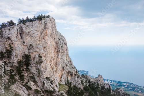 A picturesque mountain with a flat top covered with trees on the background of clouds and a misty valley with the sea far below © Sergey