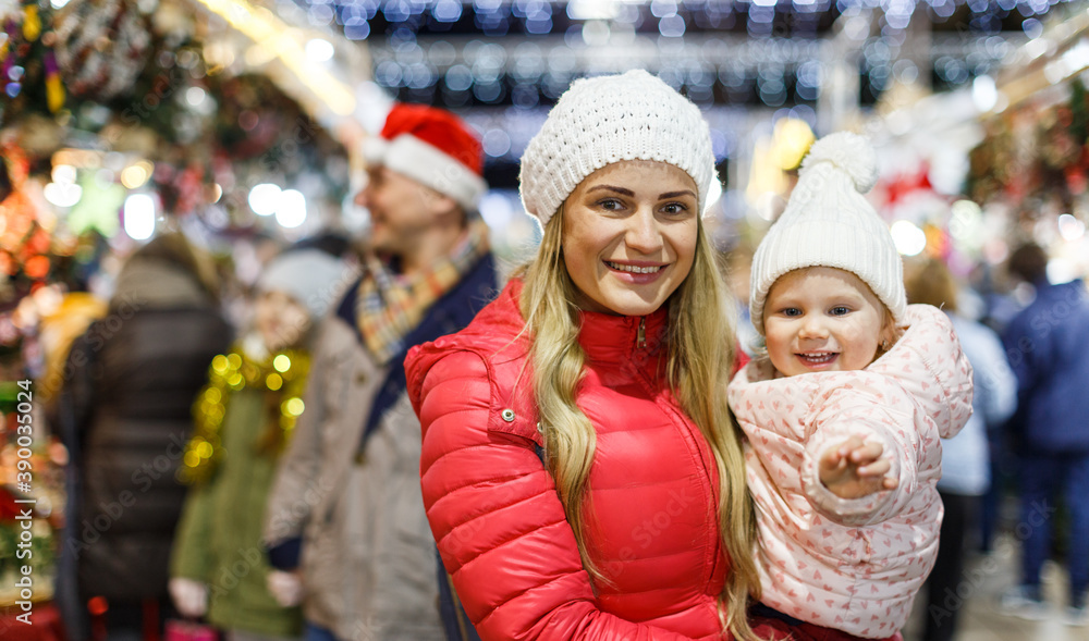 Portrait of happy young woman and her little daughter spending time at Christmas fair