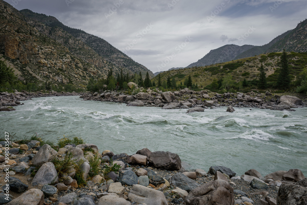 Rapid flow of water in mountain river on the background of rocks and overcast sky. Area for rafting, high level of difficulty.