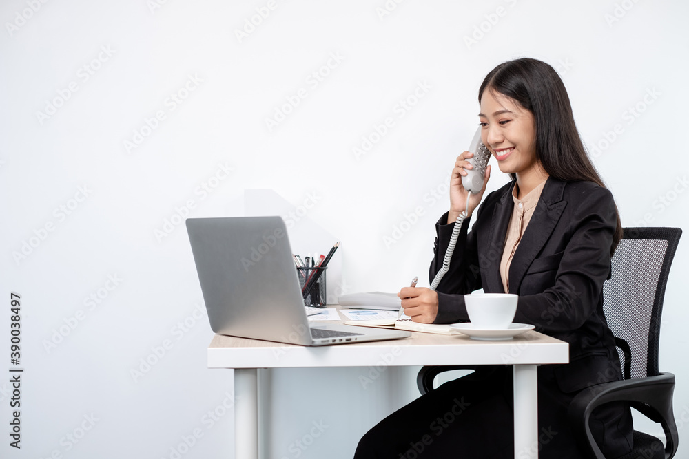 Asian businesswoman talking on the phone and working on a laptop with a cheerful and happy smile while working at the office Asian businesswoman talking on the phone and working on a laptop with a cheerful and happy smile while working at the office