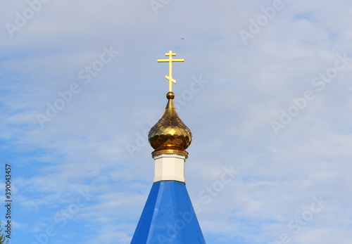 Orthodox Christian church with blue roof, golden dome and cross in Russia. A building for religious ceremonies with a bell tower against a cloudy sky