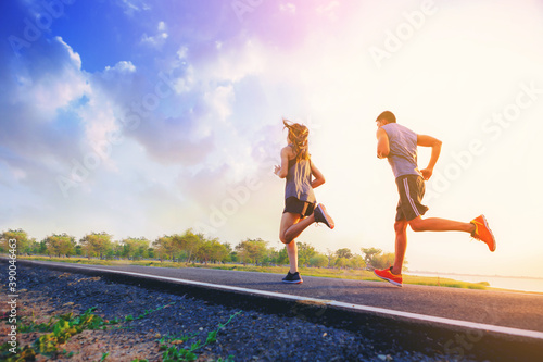 Young couples running sprinting on road. Fit runner fitness runner during outdoor workout with sunset background.
