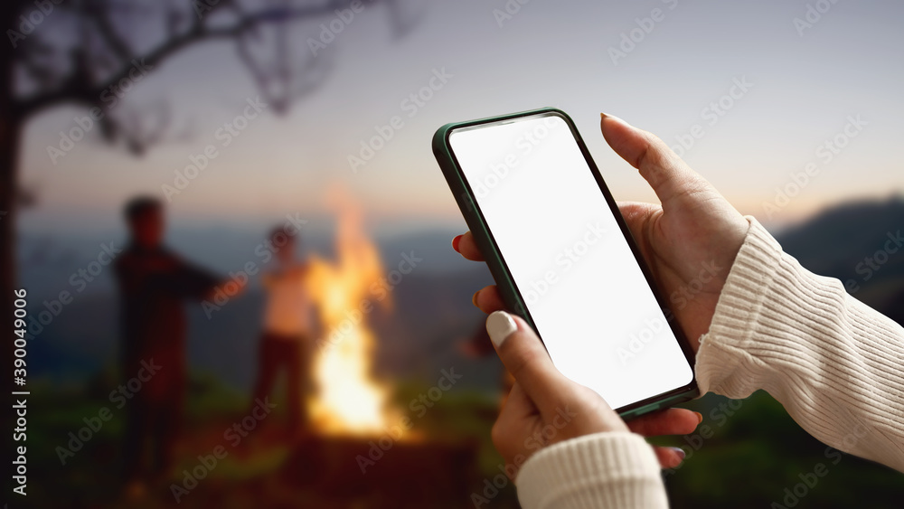 Female tourist hands holding smartphone and rest at night camping in the mountains beside campfire. - obrazy, fototapety, plakaty 