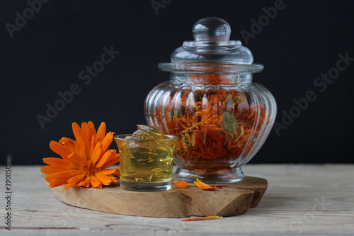 Natural cream with calendula extract and a beautiful glass jar with dried calendula flowers in the background.