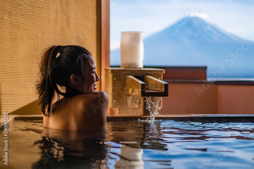 Beautiful woman enjoy onsen (mineral hot bath) in morning and seeing view of Fuji mountain in japan