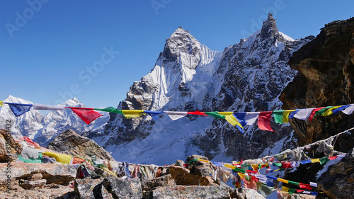 Colorful Buddhist prayer flags peacefully waving in the cold wind on the summit of Renjo La pass, Himalayas, Nepal with ice-capped mountains in background on the Three Passes Trek.