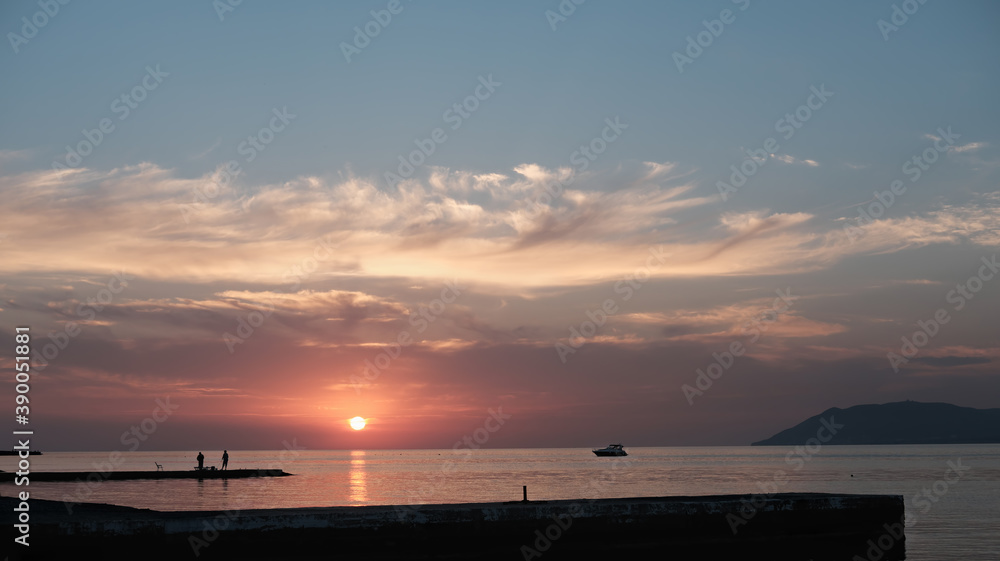 sunset at sea with boat at horizon. time before dusk. seaside landscape with men silouettes. travel destinations. beautiful evening sky with clouds.