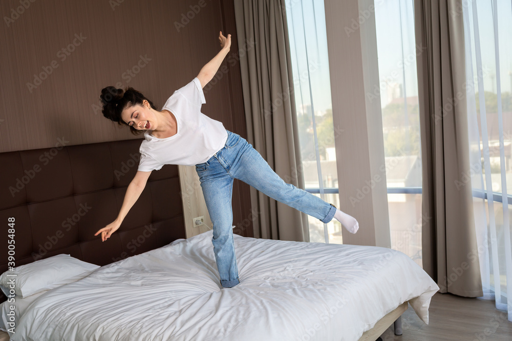 Happy young woman dancing on the bed in the bedroom. Windows on the background. Top view Happy young woman dancing on the bed in the bedroom. Windows on the background. Top view