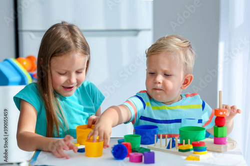 Sister helps little brother to assemble the pyramid. Educational logical toys for children. Montessori games for child development.