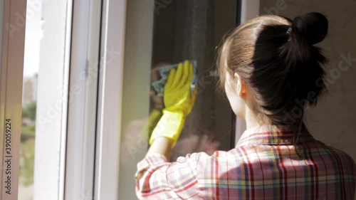 Back view of young woman cleaning dirty window in apartment and spraying cleaner and using rag  photo