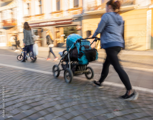 Fototapeta Naklejka Na Ścianę i Meble -  Young mother with small child in the stroller walking down the street. Intentional motion blur. Defocused image