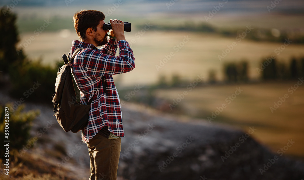 Guy looking at binoculars in hill. man in t-shirt with backpack. Guy looking at binoculars in hill. man in t-shirt with backpack.