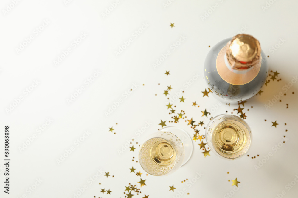 Bottle and glasses of champagne and glitter on white background