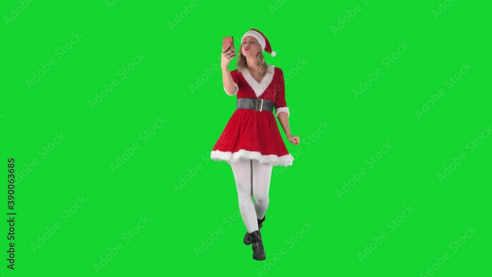 Modern Santa Claus girl walking and taking selfie photos kissing and waving at cellphone. Full body length on green screen background. Modern Santa Claus girl walking and taking selfie photos kissing and waving at cellphone. Full body length on green screen background.