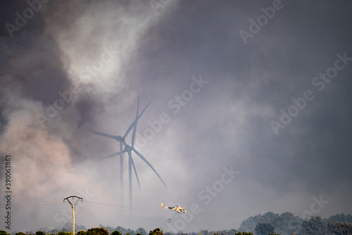 Slika na platnu Smoke, windmills and helicopter flying with bambi-bucket