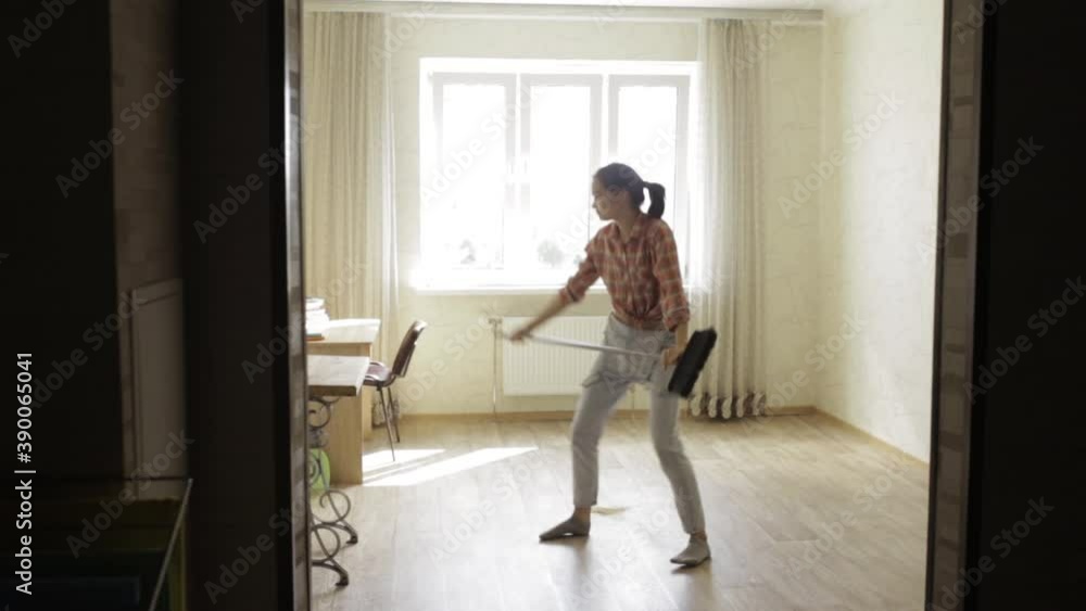 Positive woman dancing and singing with broom in room during housework and having fun Positive woman dancing and singing with broom in room during housework and having fun