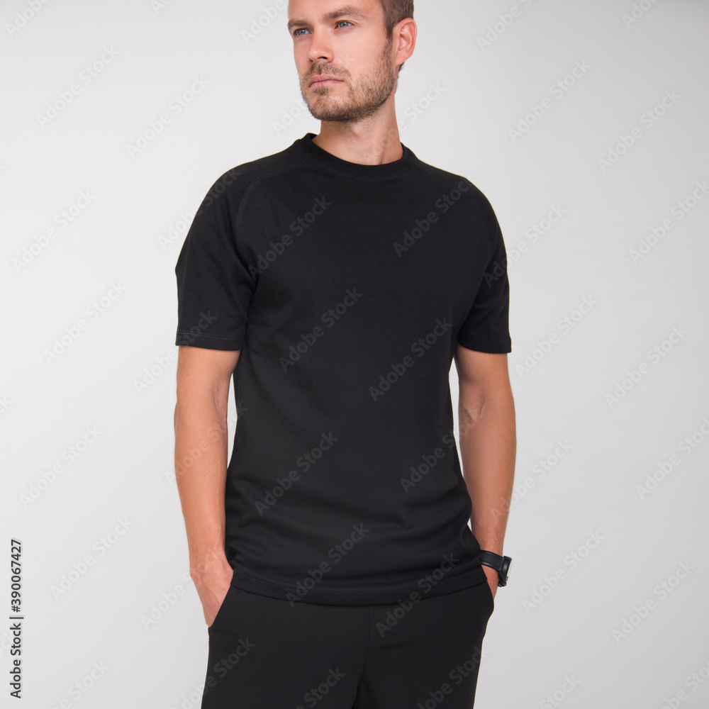 young stylish guy in black t-shirt and black pants is standing straight and looking away on the white wall background. medical concept. free space , mockup young stylish guy in black t-shirt and black pants is standing straight and looking away on the white wall background. medical concept. free space , mockup