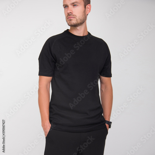 young stylish guy in black t-shirt and black pants is standing straight and looking away on the white wall background. medical concept. free space , mockup photo