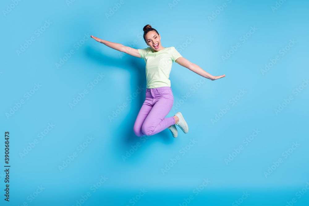 Full length body size photo of young girl jumping high laughing keeping hands like plane isolated on vibrant blue color background
