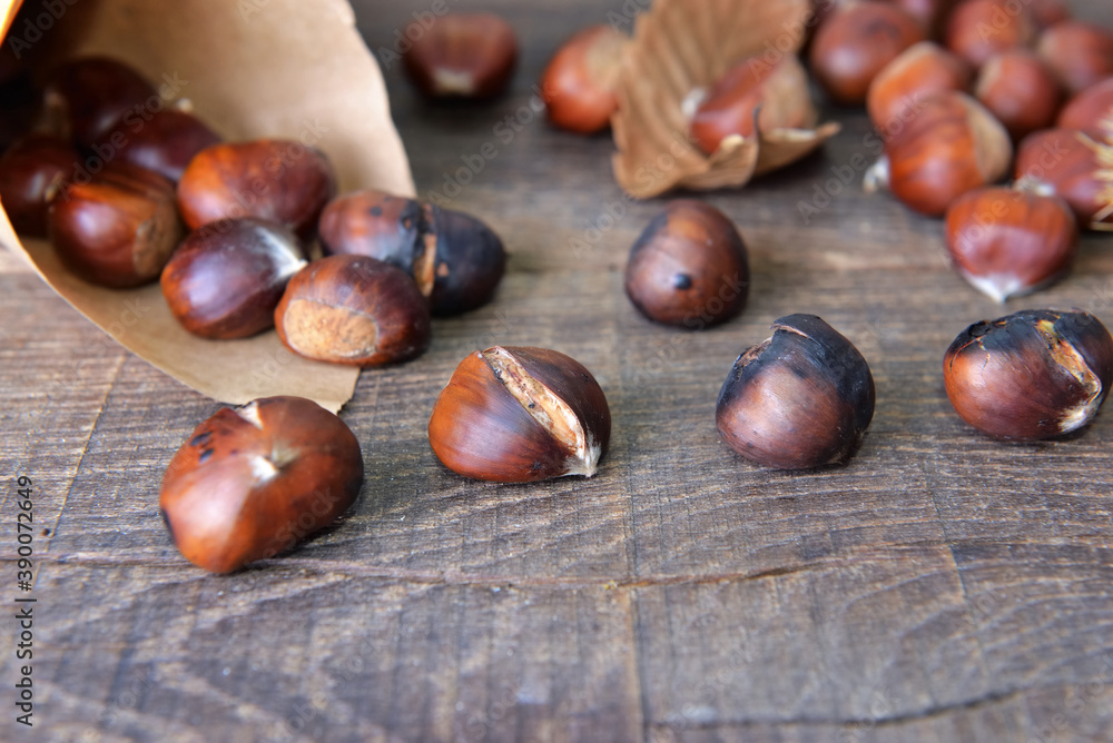 roasted chestnuts in a papaer bag spilled on wooden table roasted chestnuts in a papaer bag spilled on wooden table