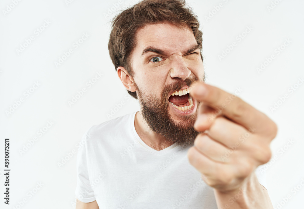 A bearded man in a white T-shirt gestures with his hands on a light background A bearded man in a white T-shirt gestures with his hands on a light background