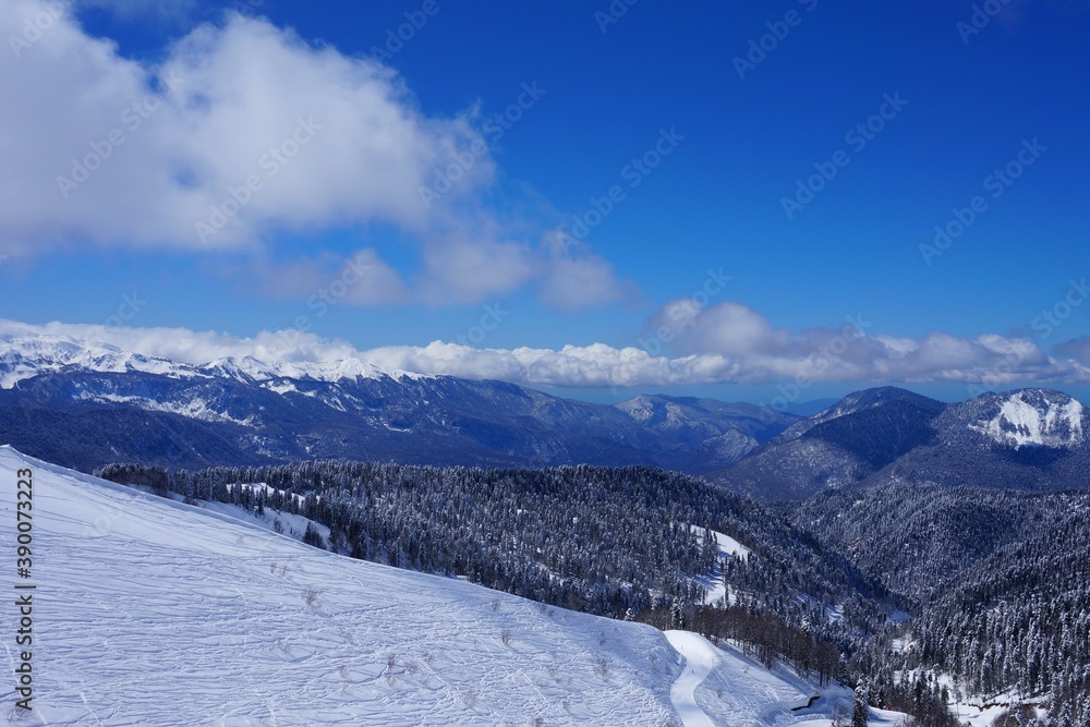 Beautiful winter landscape in the mountains, deep snow, blue sky, ski slopes, winter forest, snow-capped mountain peaks.