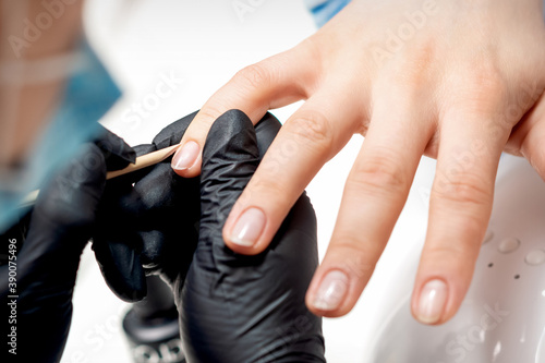 Closeup of manicurist removes cuticles on female nails by wooden orange stick in nail salon