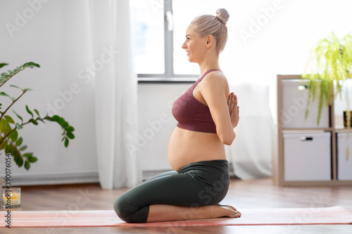 sport and people concept - happy pregnant woman doing yoga at home