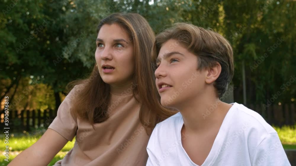 Two Caucasian, beautiful teenagers sitting on the grass talking and laughing. A boy and a girl are playing games. Free time. Two Caucasian, beautiful teenagers sitting on the grass talking and laughing. A boy and a girl are playing games. Free time.
