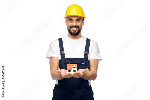 profession, construction and building - happy smiling male worker or builder in yellow helmet and overall holding model of living house over white background