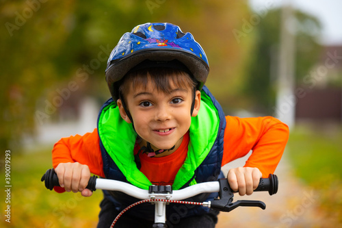 Portrait of a boy posing and smiling in a helmet and on a bicycle pedal in an autumn park. Active healthy outdoor sports