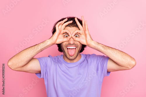 Photo of crazy guy fingers spectacles tongue out wear violet t-shirt isolated pastel pink color background