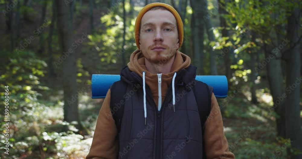Close up portrait of young man standing in forest. Male tourist looking at camera on background of woods landscape. Concept of people traveling in nature. Hiker Journey in Wildlife Close up portrait of young man standing in forest. Male tourist looking at camera on background of woods landscape. Concept of people traveling in nature. Hiker Journey in Wildlife