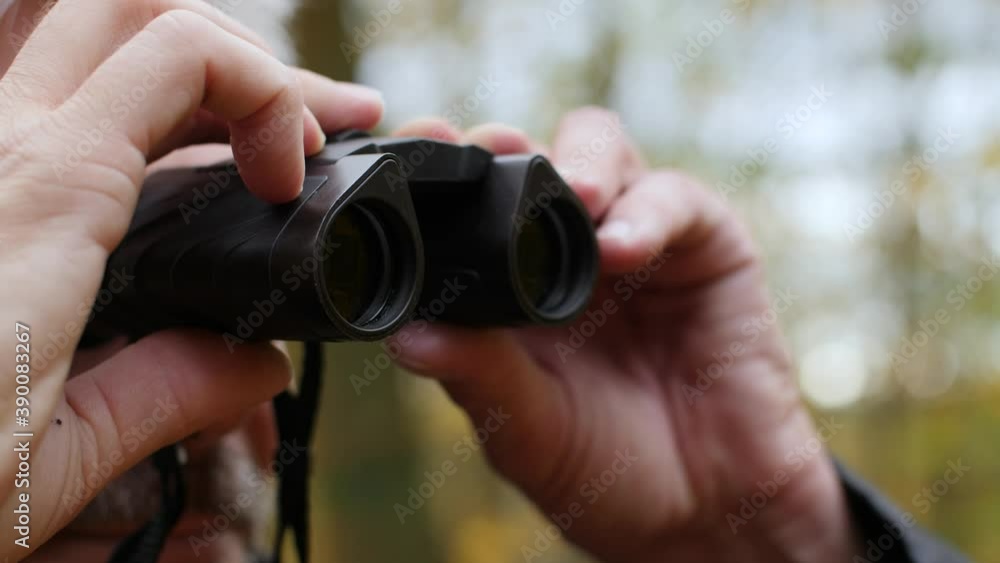 Close-up of man using binoculars in a colorful forest in late autumn. An adult watching birds outdoors and enjoying his hobby. Beautiful nature background during fall. Happy lifestyle. Close-up of man using binoculars in a colorful forest in late autumn. An adult watching birds outdoors and enjoying his hobby. Beautiful nature background during fall. Happy lifestyle.