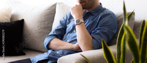 Primer plano a un hombre blanco adulto sentado sobre un sofá gris en una blanca y brillante habitación pensando y preocupado durante una jornada de trabajo en la oficina