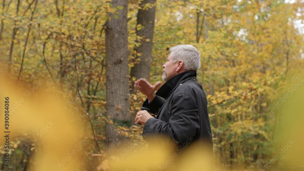 Mature middle-aged white man using binoculars in a scenic forest in late autumn. Handsome guy watches birds outdoors and enjoys his hobby. Beautiful nature background during fall. Happy lifestyle. Mature middle-aged white man using binoculars in a scenic forest in late autumn. Handsome guy watches birds outdoors and enjoys his hobby. Beautiful nature background during fall. Happy lifestyle.