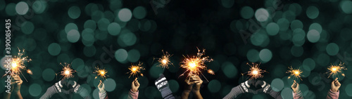 New Year / Silvester Party background banner greeting card - Group of happy people / family holding sparkling sparklers in her hands at dark night, with turquoise bokeh lights