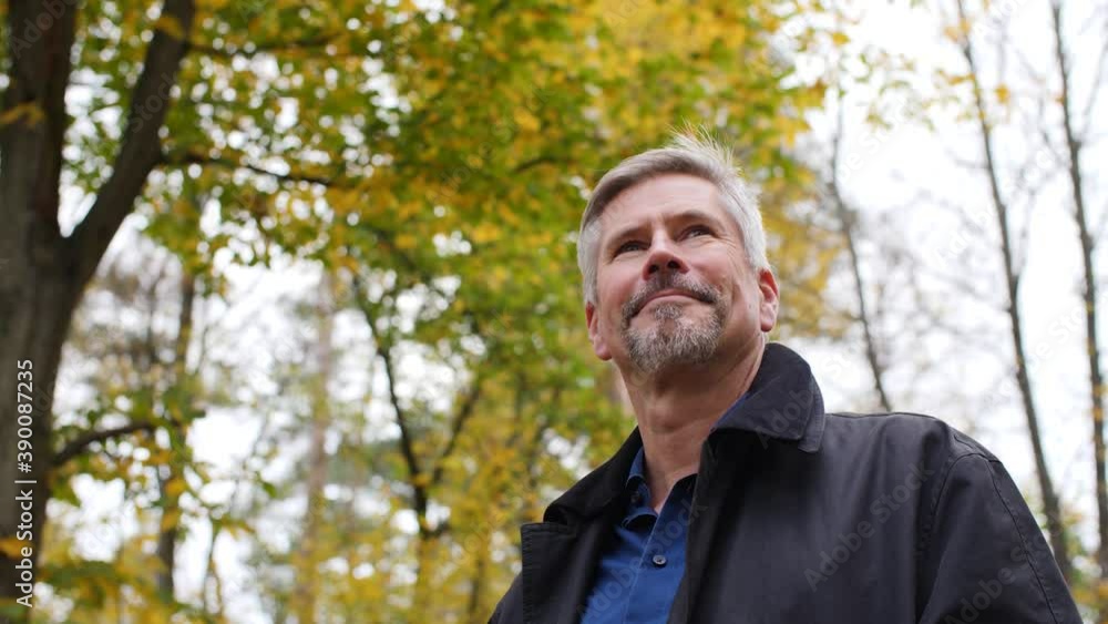 Handsome middle-aged white man looking around in a scenic forest in late autumn. Mature caucasian man relaxes in nature and enjoys his life. Beautiful colored background during fall. Happy lifestyle. Handsome middle-aged white man looking around in a scenic forest in late autumn. Mature caucasian man relaxes in nature and enjoys his life. Beautiful colored background during fall. Happy lifestyle.