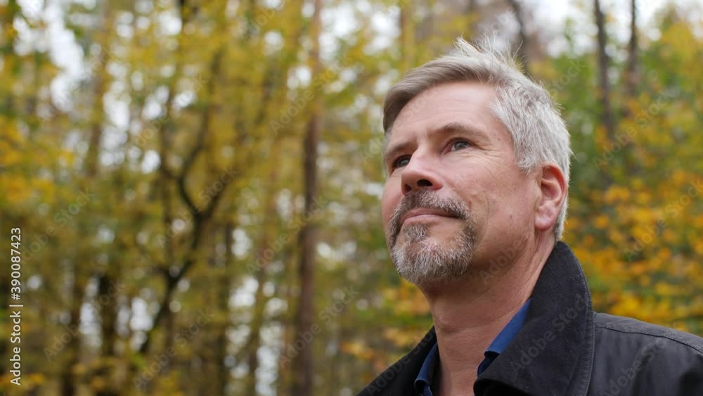 Handsome middle-aged white man looking around in a scenic forest in late autumn. Mature caucasian man relaxes in nature and enjoys his life. Beautiful colored background during fall. Happy lifestyle. Handsome middle-aged white man looking around in a scenic forest in late autumn. Mature caucasian man relaxes in nature and enjoys his life. Beautiful colored background during fall. Happy lifestyle.