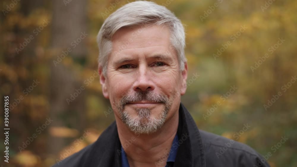 Portrait of a smiling handsome middle aged man in nature, slow motion. Mature caucasian man showing real emotions being happy, confident and likable. Attractive autumn forest background. Portrait of a smiling handsome middle aged man in nature, slow motion. Mature caucasian man showing real emotions being happy, confident and likable. Attractive autumn forest background.
