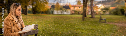 Panorama young woman sitting in the park on a bench and reading a book. In the background are beautiful autumn colors.