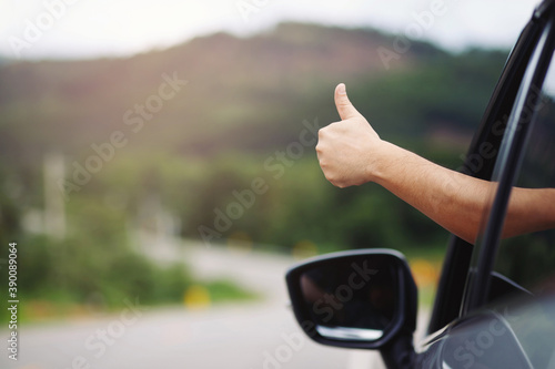 Close up people traveler hand relaxing and enjoying road trip holding thumbs up. Happy go to travel , Car on asphalt in nature, summer time. Vacation and Getaway concept.