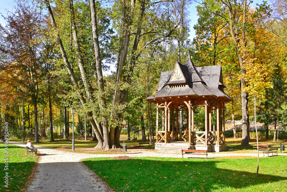Wooden structure gazebo in a spa park. Relaxing place with a pavilion with bench. Full of autumn plants and trees, a good place where spend time to rest.