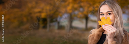 Panorama young happy woman with a smile holds an autumn yellow leaf near the face.