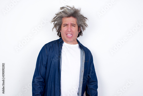 Body language. Disgusted stressed out Handsome middle aged Caucasian man with afro gray hair, against white wall, , frowning face, demonstrating aversion to something.