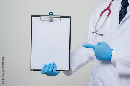 Close up Asian bald Doctor in white coat, stethoscope, blue glove wearing face mask pointing finger to paper on clipboard isolated on white background.