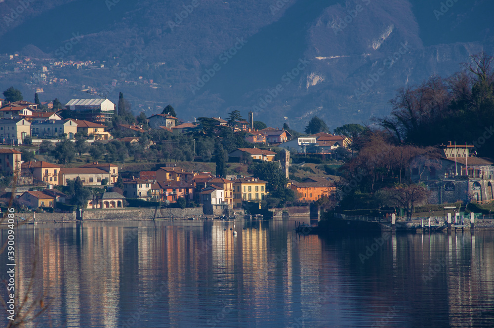 Reflections on the calm water of the lake of winter colors of sunny villages.Como lake, lombardy, Italy