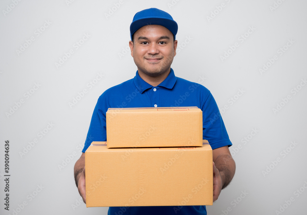 Young smiling asian delivery man in blue uniform holding box parcel cardboard on isolated white background. Young smiling asian delivery man in blue uniform holding box parcel cardboard on isolated white background.