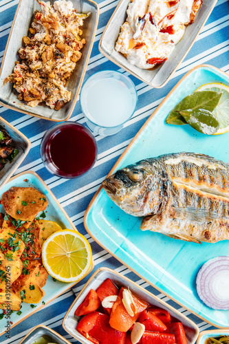 Fototapeta Naklejka Na Ścianę i Meble -  Grilled fish, salads and vegetables. Seafoods, grilled meat, meze, raki, ouzo, appetizers and salads on the table in Greek or Turkish Fish Restaurant for dinner or lunch at the beach.