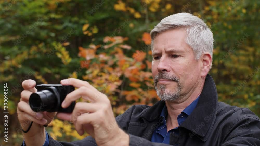 Mature middle-aged white man taking pictures in a scenic forest in late autumn. Handsome male photographer travels outdoors with a small camera. Beautiful nature background during fall. Happy tourist. Mature middle-aged white man taking pictures in a scenic forest in late autumn. Handsome male photographer travels outdoors with a small camera. Beautiful nature background during fall. Happy tourist.